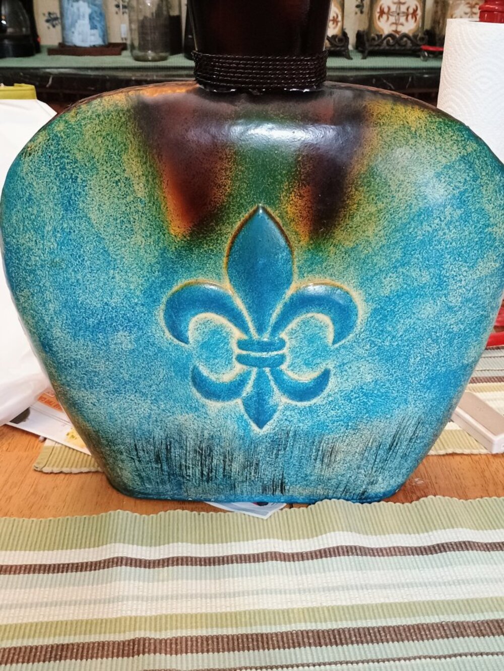 This is a teal and brown metal vase with a fleur-de-lis design